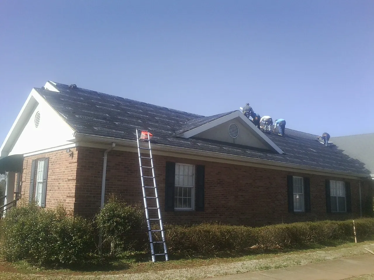 Crew tearing shingles off a brick ranch roof with a ladder set — Metal Roof Repair work by our crew in Leeton
