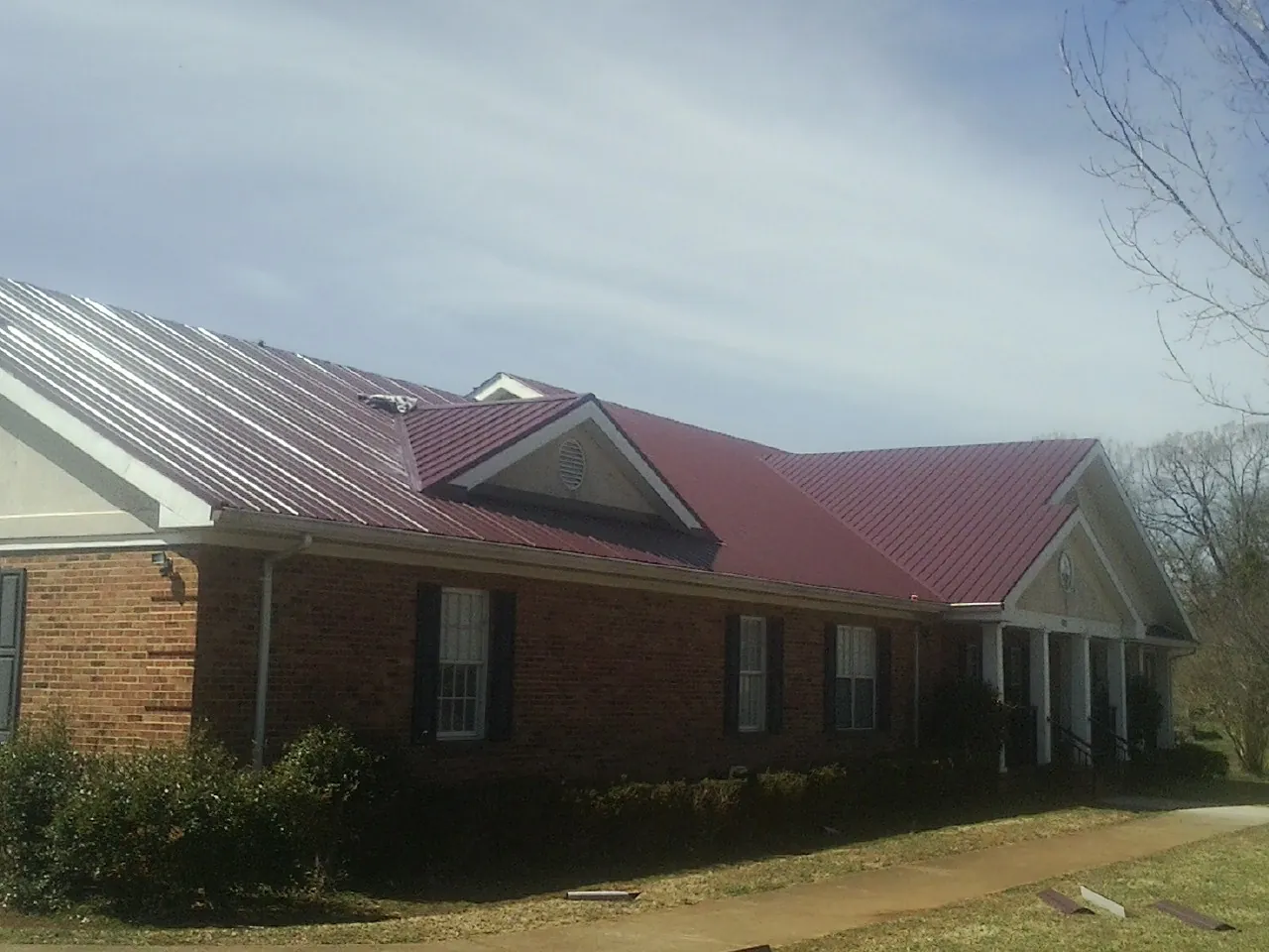 Red metal roof with gabled entries on a long brick building, from a Hail Damage Roof Repair job in Leeton