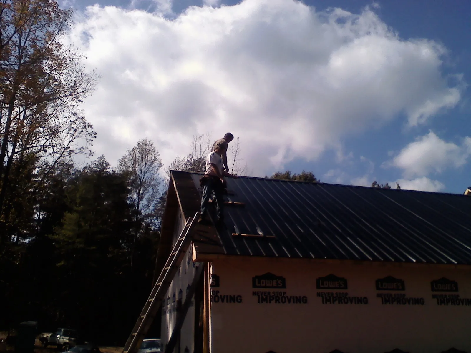 Roofer fastening dark metal panels high against a cloudy sky, from a Roof Inspection job in Leeton
